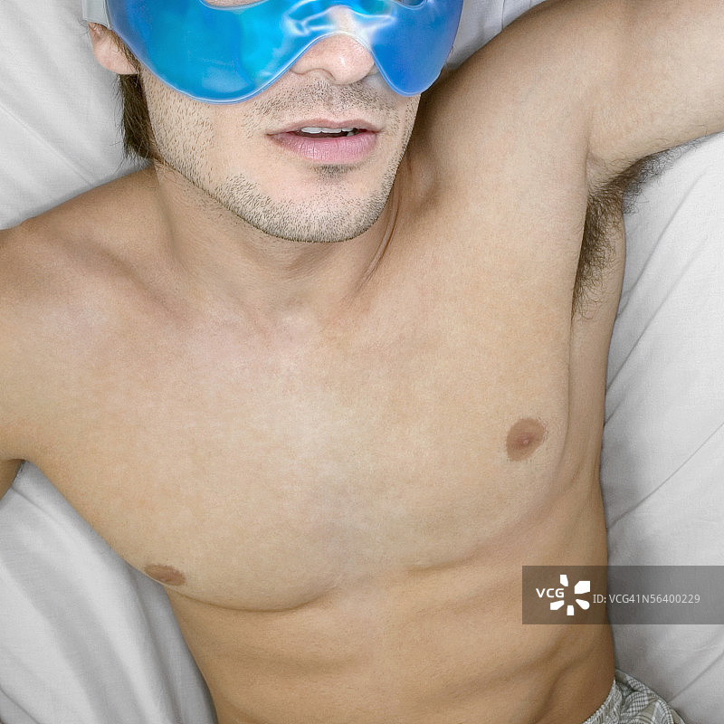 青年男子躺在床上，伸展双臂，眼睛上戴着蓝色凝胶眼罩图片素材