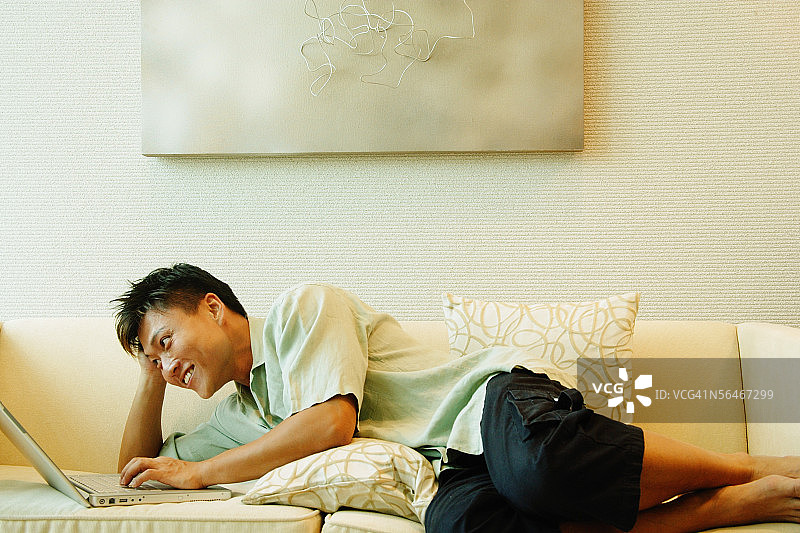 男人躺在沙发上使用笔记本电脑图片素材