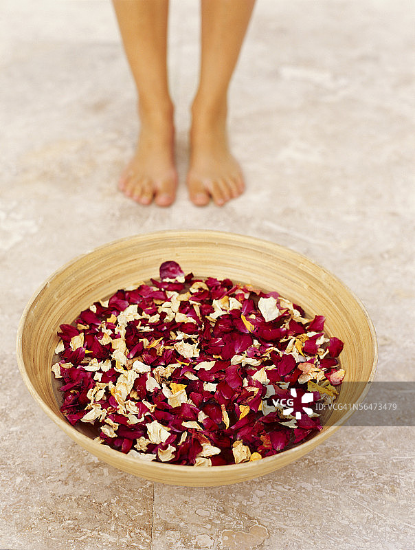 装有玫瑰花瓣的碗后的人的脚的俯视图图片素材
