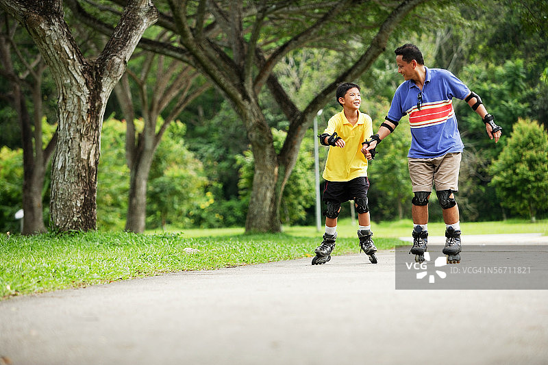 在公园里玩轮滑的父子，父亲牵着儿子的手图片素材