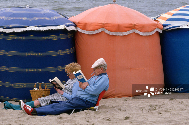 在法国特鲁维尔，情侣在海滩帐篷旁阅读图片素材