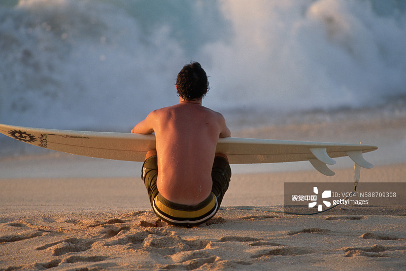 冲浪者坐在海滩上拿着冲浪板图片素材