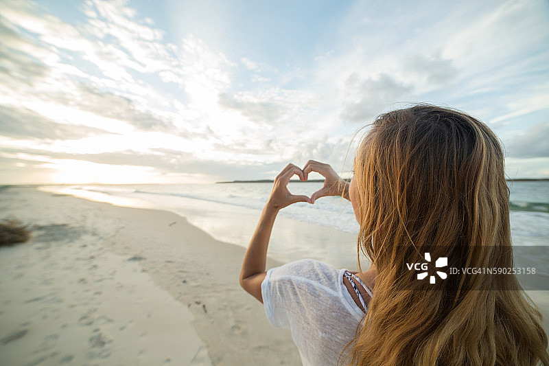 年轻女子在海滩上用手将日落框成心形图片素材