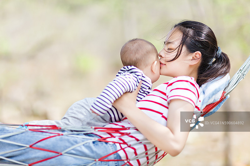 年轻母亲在自然背景下拥抱吊床上的婴儿图片素材