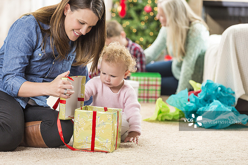 母亲帮助蹒跚学步的女儿打开圣诞礼物图片素材