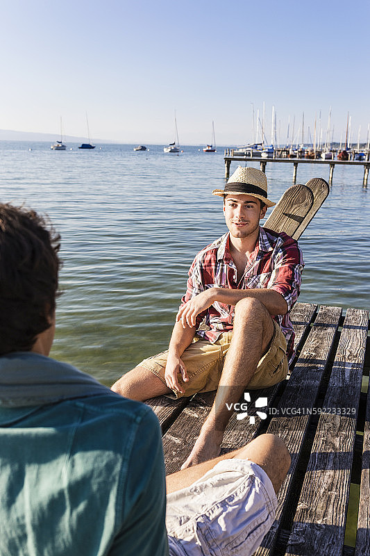 朋友们坐在德国巴伐利亚阿莫尔湖畔的木制码头上图片素材