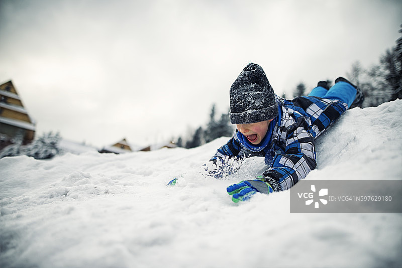 冬日里，小男孩从山上滑下来图片素材