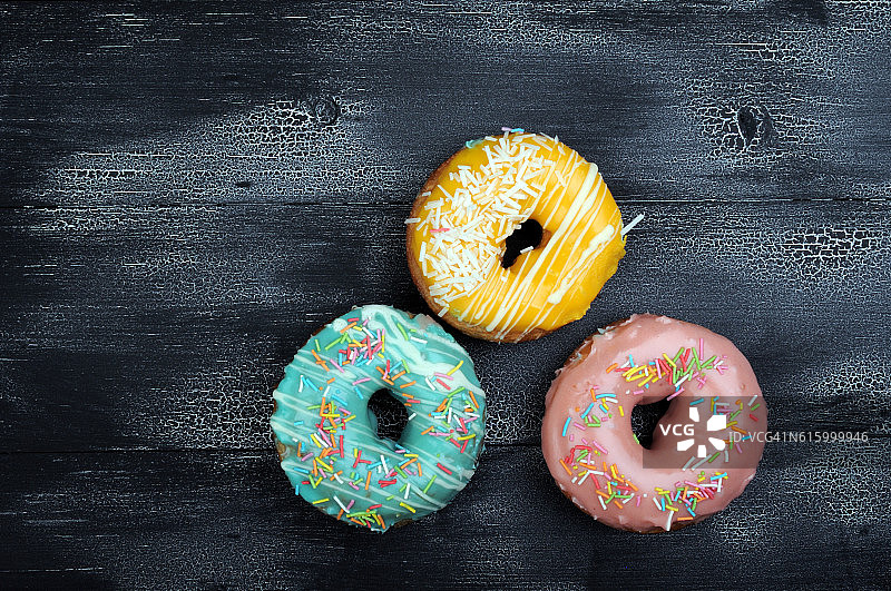 黑色木质背景上的彩色甜甜圈图片素材