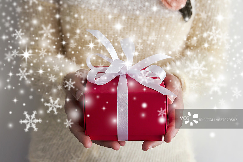 年轻女人的手捧着红色礼品盒，有雪花图片素材