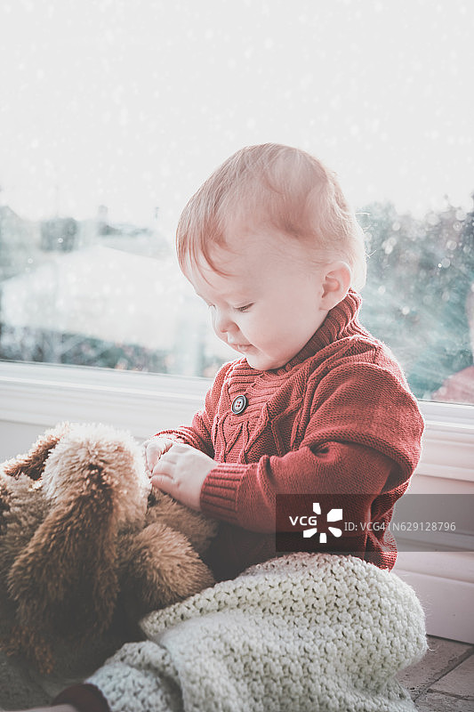 冬季窗边抱着毛绒狗玩具的男婴图片素材