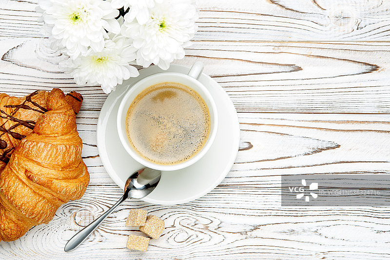木制背景上的两份新鲜羊角面包、咖啡和鲜花图片素材