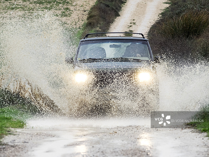 在泥泞道路上飞溅过大水洼的四驱车，西班牙图片素材
