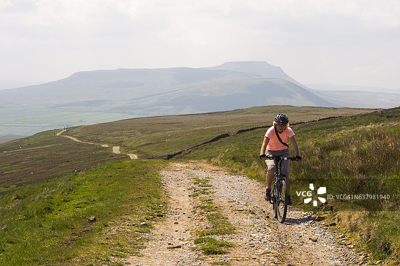 女人在英国约克郡山谷Ribble Head上方的Cam路上骑山地自行车图片素材