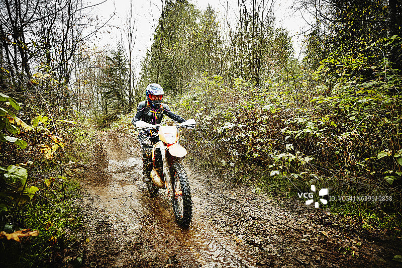 女摩托车手骑越野摩托车穿过泥泞的森林小径图片素材
