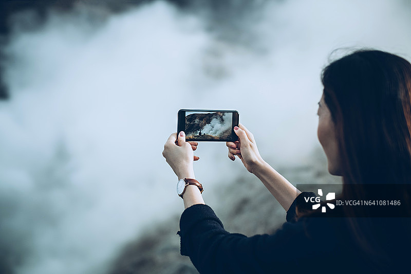 年轻女子用手机拍摄温泉山美景图片素材