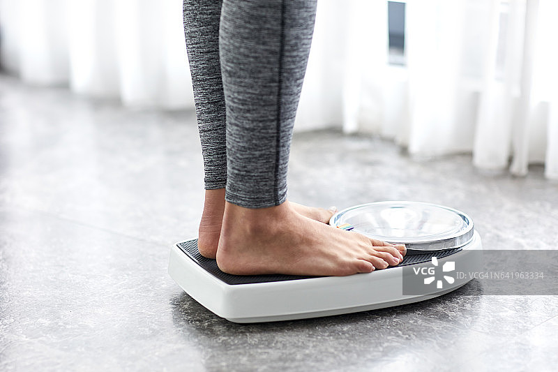 年轻健康的女孩站在家用体重秤上图片素材