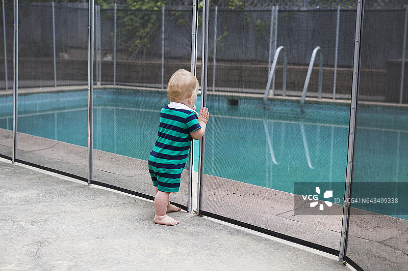 幼儿透过栅栏的裂缝看着游泳池图片素材
