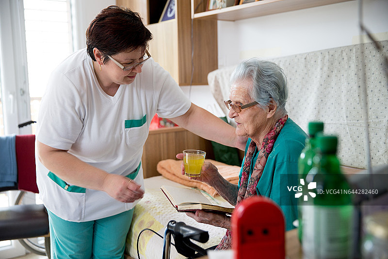 护理人员给老年中心的年长女性送饮料图片素材