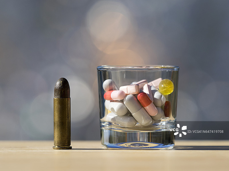 阳光照射下装满过量药物和子弹的玻璃杯图片素材