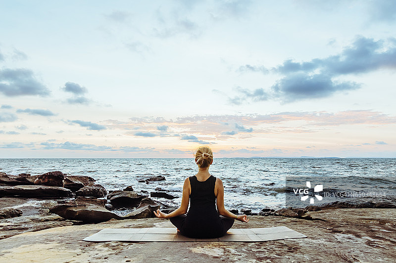 年轻女子在海边悬崖上做瑜伽动作图片素材