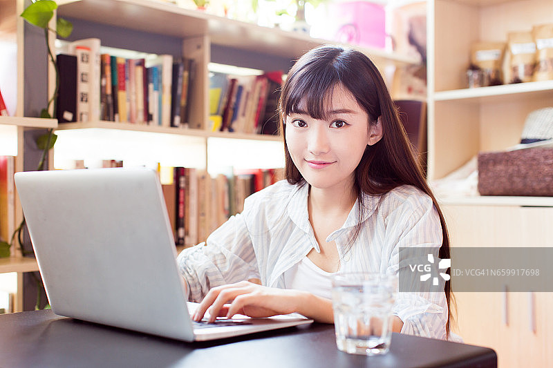 在书店用笔记本电脑学习的微笑女学生图片素材