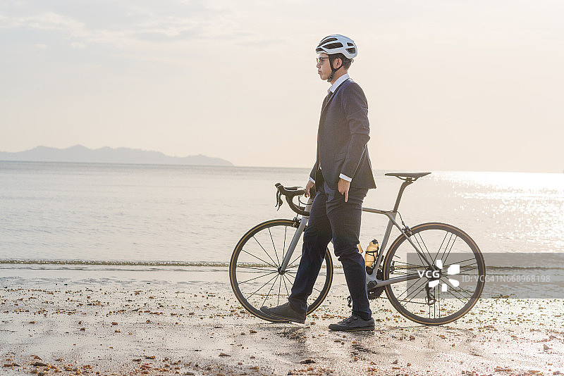 年轻的亚洲商务男人在日落时于海滩骑自行车放松身心图片素材
