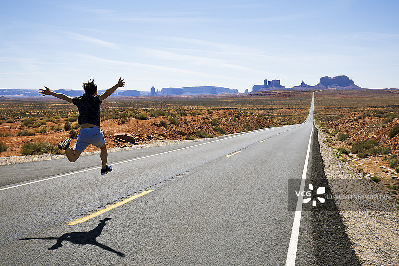 男人在美国犹他州纪念碑谷163号公路跑步和跳跃图片素材