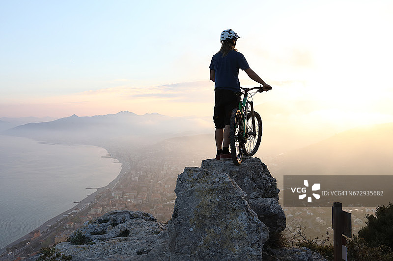 年轻人骑山地自行车在山顶岩石上休息，下方是海图片素材