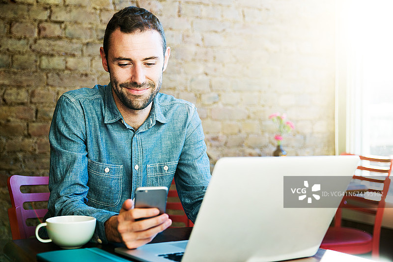 在咖啡店里使用手机和笔记本电脑的男子图片素材