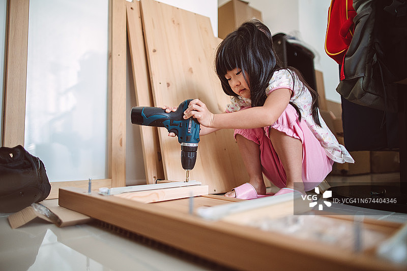 可爱的小女孩自己用电动螺丝刀组装家具图片素材