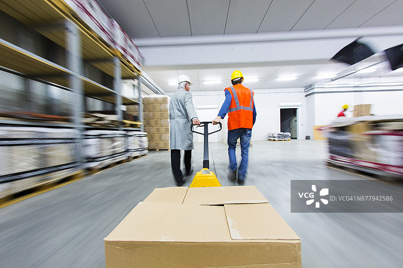 两名仓库工人拉着装满箱子的托盘车图片素材