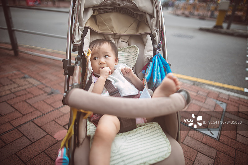 可爱的小宝宝坐在婴儿车里，正把手放进嘴里图片素材