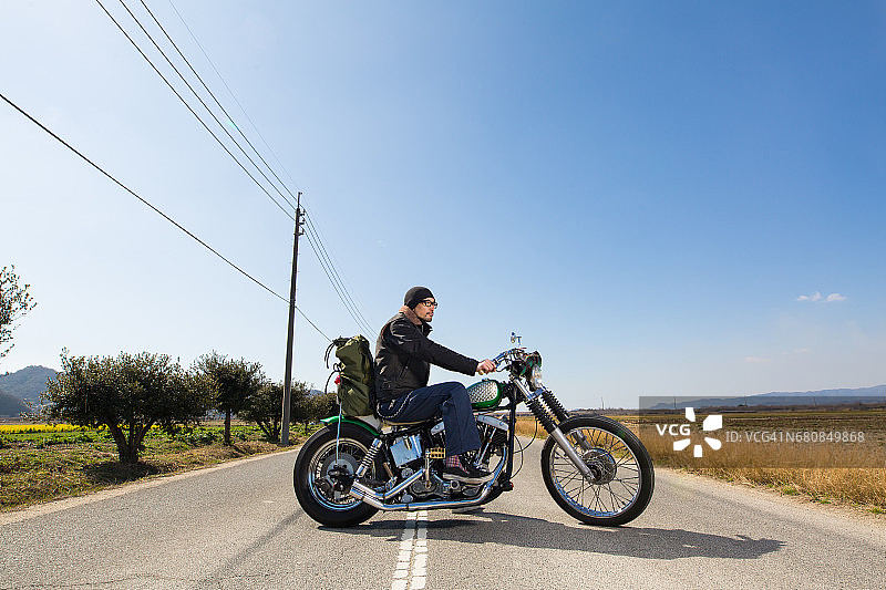 男人坐在沙漠公路中央的定制摩托车上图片素材