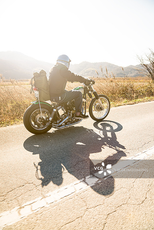一个日本男人骑着他的定制摩托车在阳光下沿着荒凉的道路行驶图片素材
