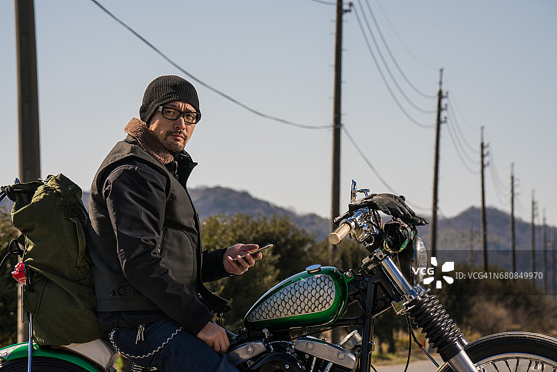 一名男子在沙漠中坐在定制摩托车上使用智能手机图片素材