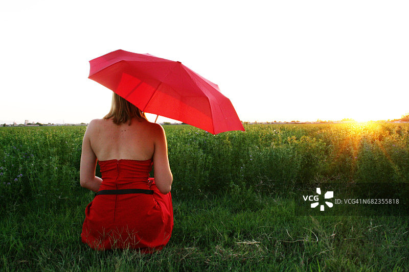 女人坐在草地上撑着红伞图片素材