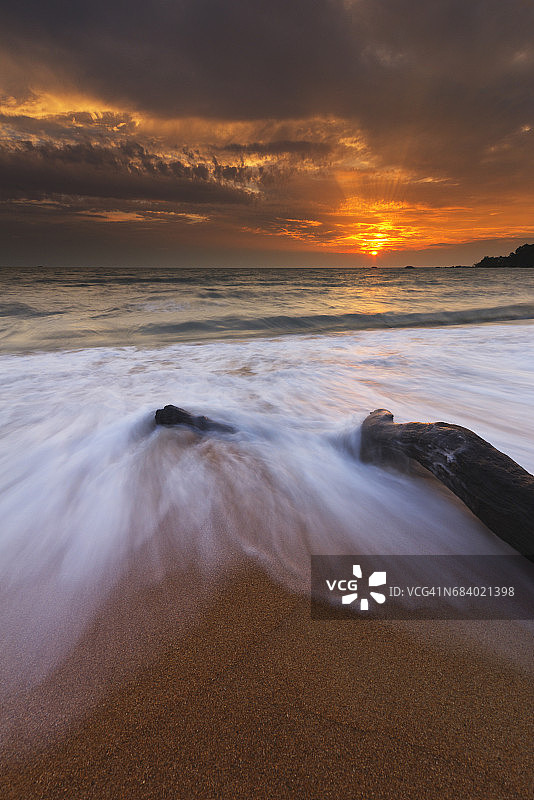 海滩上环绕枯木的海浪图案（长曝光拍摄）图片素材