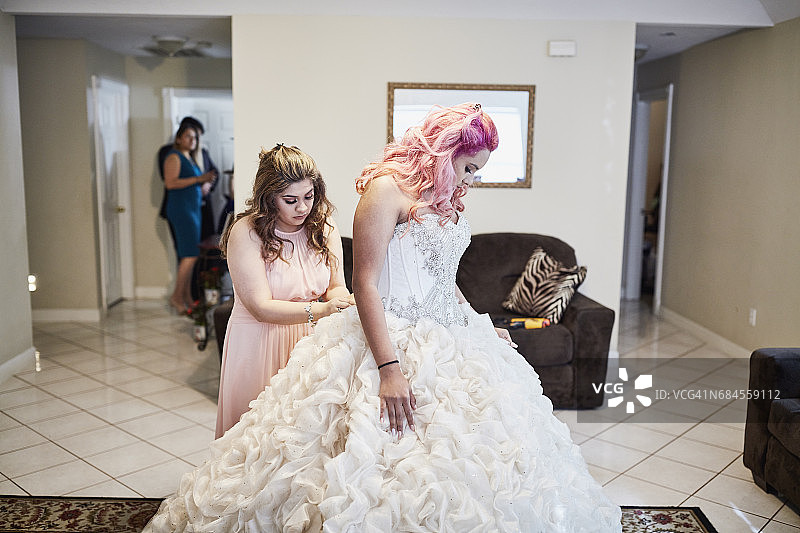 在客厅里，朋友帮年轻女人穿上成人礼服图片素材