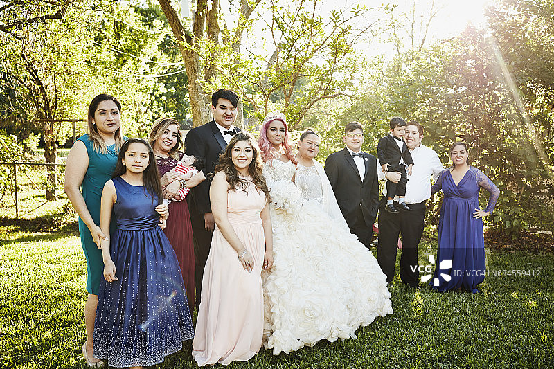 穿着 Quinceanera 礼服的年轻女子与多代同堂的家庭站在后院的肖像图片素材