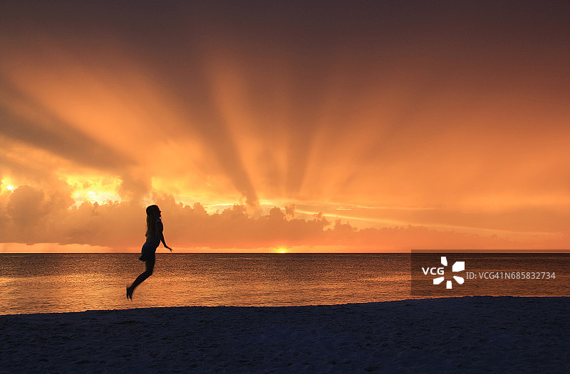 在日落时在海滩上跳跃的女人剪影图片素材