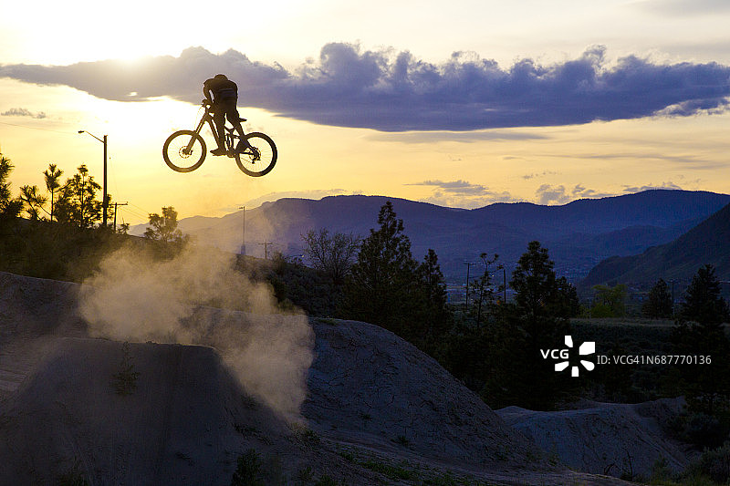 年轻男子在日落时分骑速降山地自行车飞跃图片素材