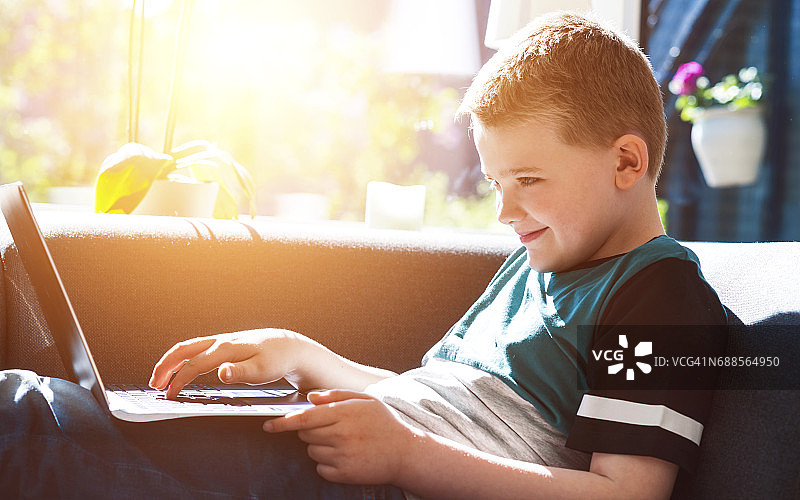 男孩坐在沙发上用笔记本电脑打字图片素材