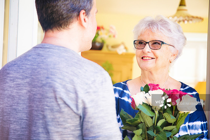 老年妇女对着拿着玫瑰花束的中年儿子温暖地微笑图片素材