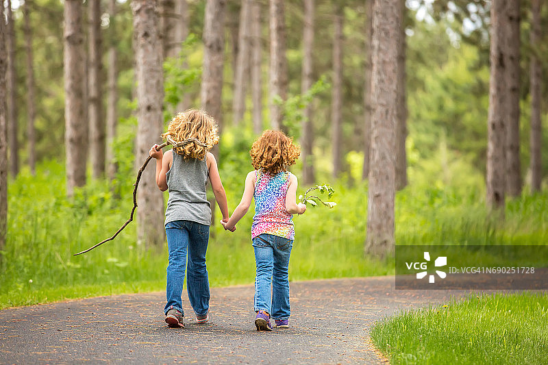 两个小女孩在铺好的小路上穿过树林图片素材