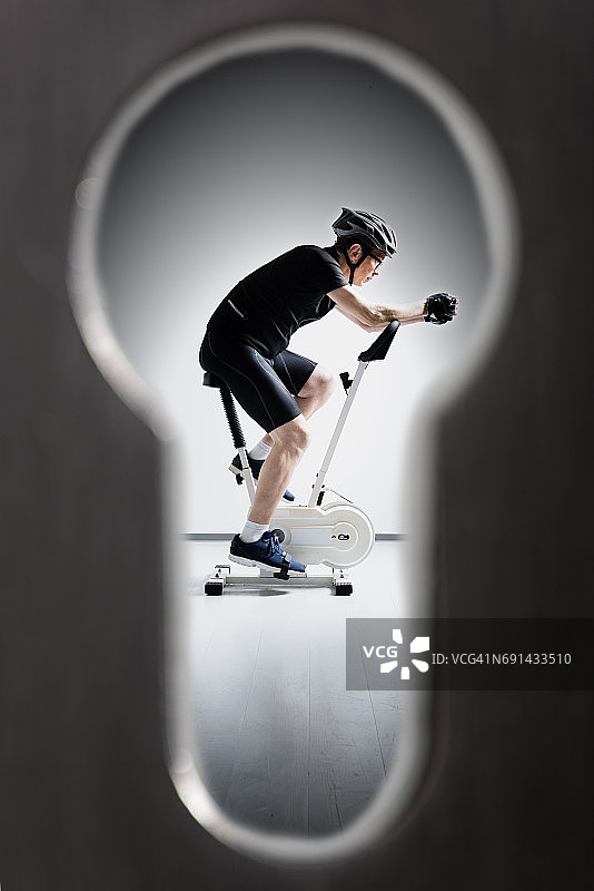 透过钥匙孔窥视骑健身自行车的家伙图片素材