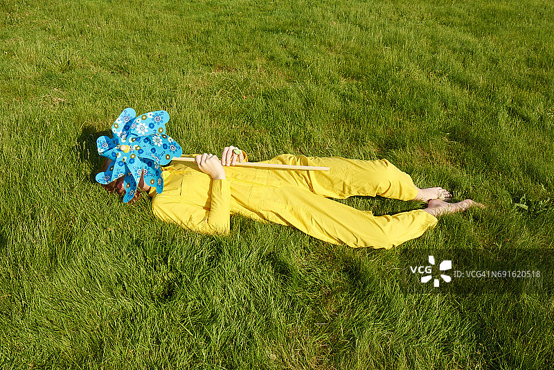穿着黄色连体裤的女孩在草地上玩风车图片素材
