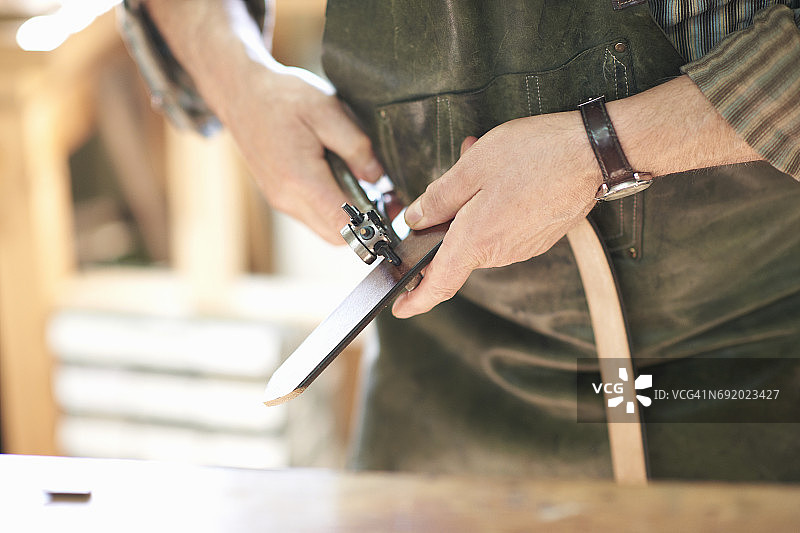 皮革作坊里的工人正在皮革腰带上打孔，中部特写图片素材