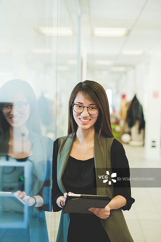 年轻女子倚靠在办公室门口使用平板电脑图片素材