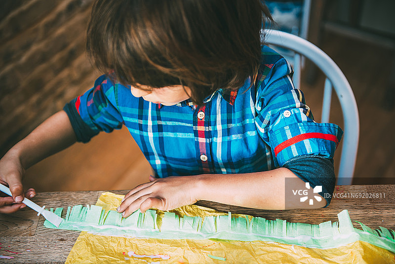 男孩在皱纹纸上涂胶水制作皮纳塔图片素材