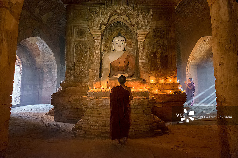 缅甸蒲甘，年轻僧侣在佛塔内佛像前点燃蜡烛祈祷图片素材